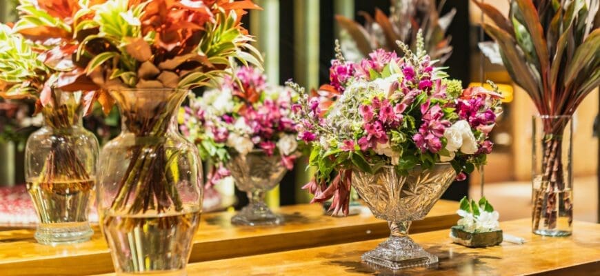 A shelf in front of a mirror with three large vases of flowers on top of it
